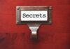 A label holder on a wooden surface with the word Secrets displayed