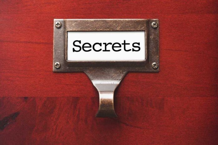 shutterstock_106336844.jpg A label holder on a wooden surface with the word Secrets displayed