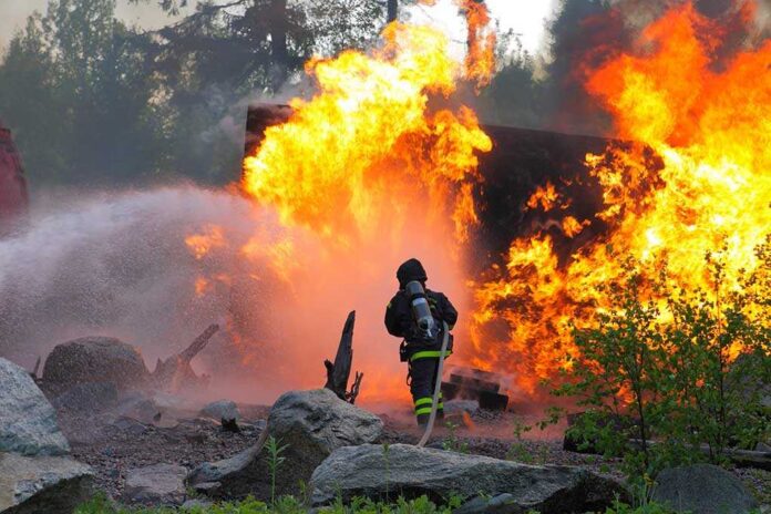 Firefighter battling a large fire with water spray