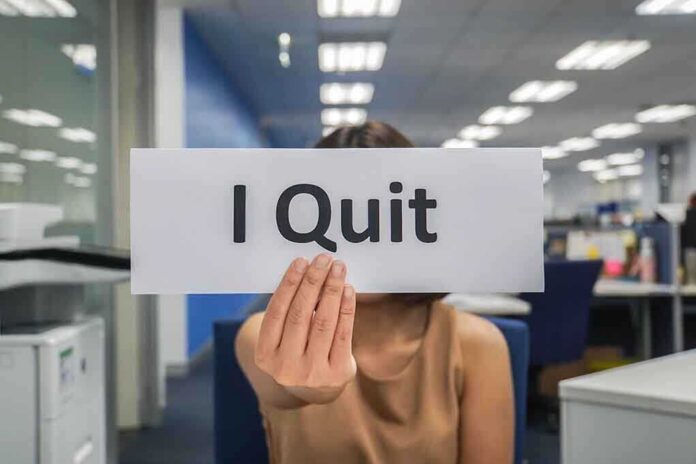 shutterstock_1119863465.jpg Person holding a sign that says I Quit in an office setting