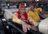 Two elderly men in military attire sitting in a classic convertible car during a parade