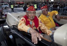 Two elderly men in military attire sitting in a classic convertible car during a parade