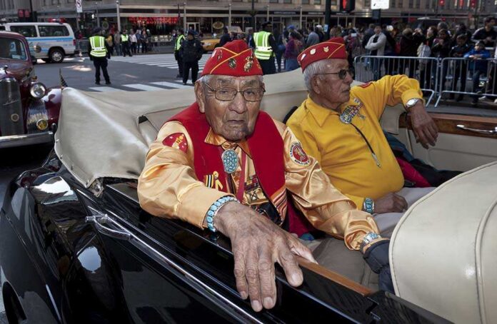 Two elderly men in military attire sitting in a classic convertible car during a parade