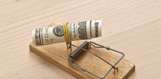 A rolled stack of cash secured in a mousetrap on a wooden surface