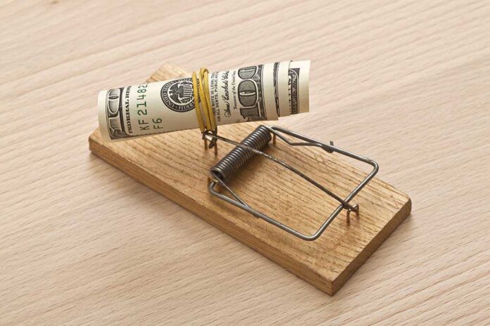 A rolled stack of cash secured in a mousetrap on a wooden surface
