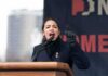 A woman passionately speaking at a podium during a rally