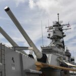 FIRE Aboard America’s Most Expensive Warship Injures Crew Close-up of a battleships naval guns and superstructure against a cloudy sky