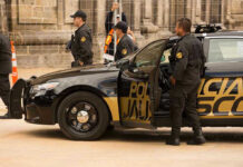 Police officers standing and sitting near a patrol car.