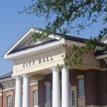 Shock Exit — Mayor Quits After Re-election Exterior view of a city hall building with columns and a clear blue sky