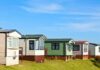 Row of colorful mobile homes on a grassy hill under a blue sky