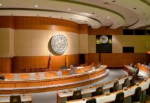 Massive Fraud Exposure: Billions at Stake! Interior view of a government chamber with wooden paneling and seating