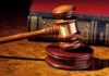 Federal Judge Charged After Parking Lot Meltdown A wooden gavel resting on a polished surface with a law book in the background