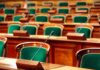 Warrantless Spying Standoff Explodes Empty legislative chamber with green upholstered chairs and wooden desks