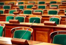 Warrantless Spying Standoff Explodes Empty legislative chamber with green upholstered chairs and wooden desks