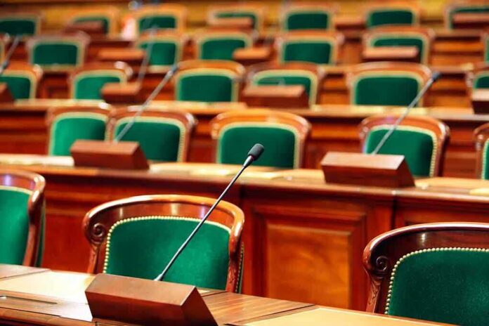 shutterstock_223257358 Empty legislative chamber with green upholstered chairs and wooden desks