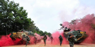 Soldiers running from armored vehicles with red smoke.