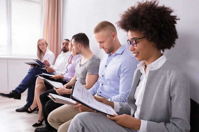 shutterstock_1158960115 Group of job applicants sitting in a row reviewing documents
