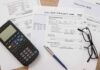 Utility bills with calculator, pen, and eyeglasses on a desk