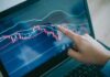 Hand pointing at stock chart on laptop screen