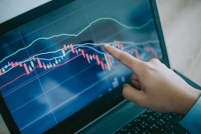 Hand pointing at stock chart on laptop screen