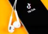 Legal Loophole Rescues TikTok Smartphone with TikTok app and white wired earbuds on yellow background