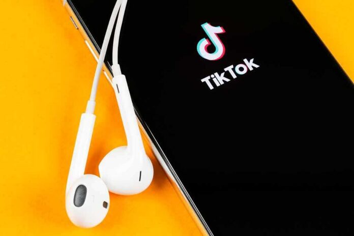 shutterstock_1388508074 Smartphone with TikTok app and white wired earbuds on yellow background