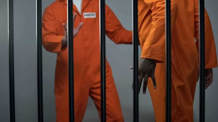 shutterstock_1486461206 Two inmates in orange jumpsuits behind jail bars