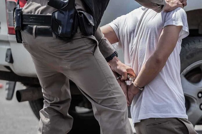 shutterstock_1705187374 police officer handcuffing a person beside a vehicle