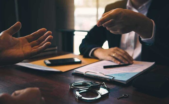 shutterstock_1728879205 Two people in discussion at a desk with handcuffs and documents
