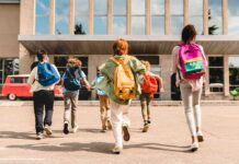 Group of schoolchildren with backpacks running toward a school entrance