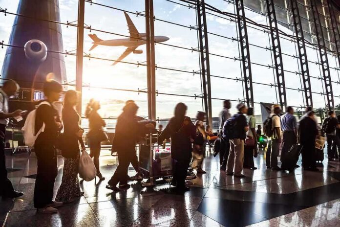 Passengers queue inside an airport terminal at sunset