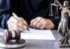 Judge writing at desk with gavel and Lady Justice statue