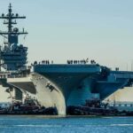 Eight Attempts Reported Across Carrier Strike Group Aircraft carrier guided by tugboats in a harbor