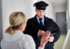 Police officer taking notes while speaking with a woman in a hallway