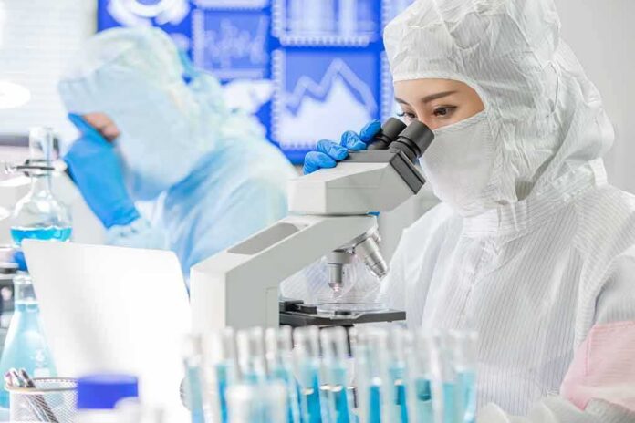 shutterstock_1545991736 Scientist in protective suit using a microscope