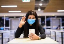 Woman in face mask video calling on smartphone in a cafeteria