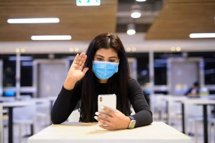 Woman in face mask video calling on smartphone in a cafeteria