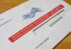 Judge Said Stop — USPS Charged Ahead Mail-in ballot envelope with red label on wooden table