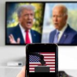 ActBlue Standoff Explodes In Federal Court Smartphone with ballot icon held before a TV showing two blurred politicians