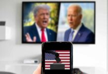 Smartphone with ballot icon held before a TV showing two blurred politicians