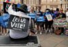 Christian Jones sits with a 'Let Us Vote' sign facing a crowd at a voting rights rally