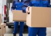 workers in blue uniforms carrying cardboard boxes from a van