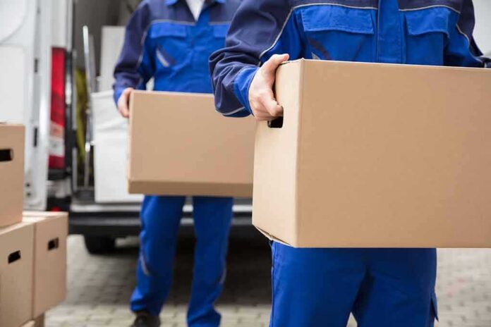 workers in blue uniforms carrying cardboard boxes from a van