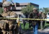 Tactical police officers behind yellow caution tape at an outdoor scene