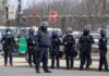 Group of police officers in riot gear standing on a street; Brian Folkerts present