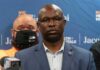 Man in suit and glasses at a press conference