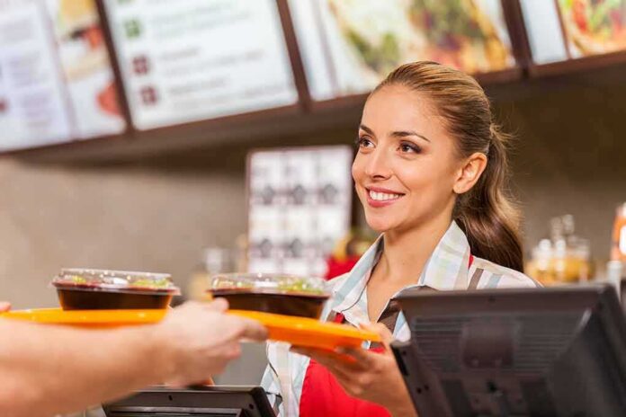Smiling cashier handing food trays to a customer