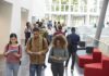 Students walking through a bright campus lobby using mobile devices