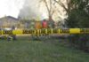 Yellow police tape marking a restricted area at a fire scene with firefighters in the background
