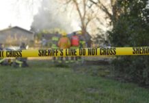 Police Royalty: Sudden Murder‑Suicide Shock Yellow police tape marking a restricted area at a fire scene with firefighters in the background